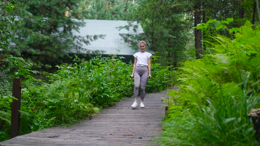Beautiful sportswoman doing squats, lunges with dumbbells in the forest, during summer outdoor recreation