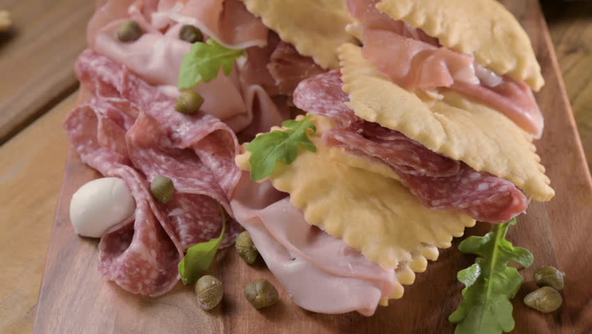 Crescentina. Food of Emilia Romagna region, deep fried bread gnocco fritto or crescentina. Starter or aperitif in Italy. Creshantina with prosciutto crudo, mortadella, Milanese salami, capers, cheese 