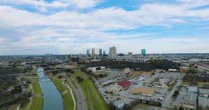 4K aerial establishing shot of the Fort Worth, Texas skyline on a partly sunny day with cars, people, highways, trains, bridges, the Trinity River, and outdoor activities.