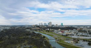 4K aerial establishing shot of the Fort Worth, Texas skyline on a partly sunny day with cars, people, highways, trains, bridges, the Trinity River, and outdoor activities.