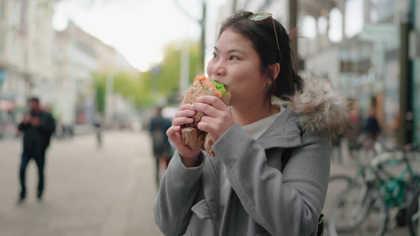 attractive young asia travel happiness woman, smiling cheerfully, holds a delicious hamburger in two hands.Happy tourist eating a burger while carefree walking tour vacation in the street