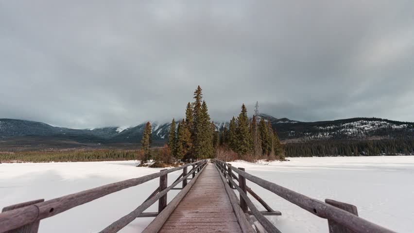 Time lapse of Snowy wooden bridge with tiny pine forest and cloudy blowing in the night at Pyramid Lake on winter in Jasper national park, Alberta, Canada