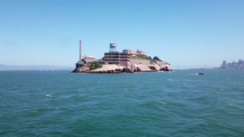 Gimbal moving shot approaching the backside of Alcatraz Island by boat with the Bay Bridge and San Francisco visible in the background. 4K