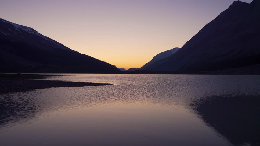 Lake shore at twilight. Colorful sky, silhouette of mountains skyline reflection on the lake water surface.