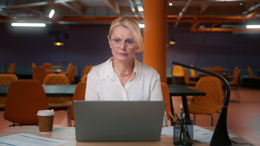Tired mature woman 50s overworked on computer late at office. Unhappy frustrated workaholic businesswoman working at project deadline overtime. Annoyed overwhelmed sad CEO boss in loft empty office 4K Royalty-Free Stock Footage #1100675311