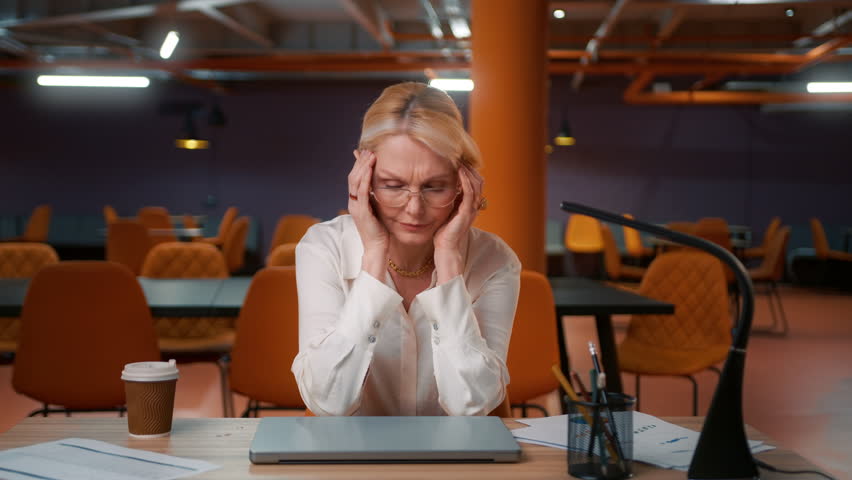 Tired mature woman 50s overworked on computer late at office. Unhappy frustrated workaholic businesswoman working at project deadline overtime. Annoyed overwhelmed sad CEO boss in loft empty office 4K | Shutterstock HD Video #1100675311