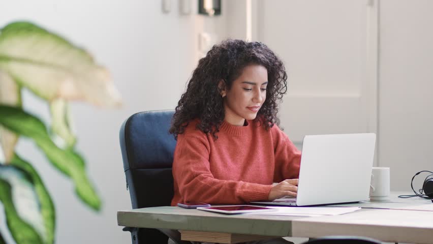 Young smiling latin professional business woman, office worker, sales manager sitting at desk using laptop, browsing searching online, working on online marketing project, typing on pc in office. Royalty-Free Stock Footage #1100677295