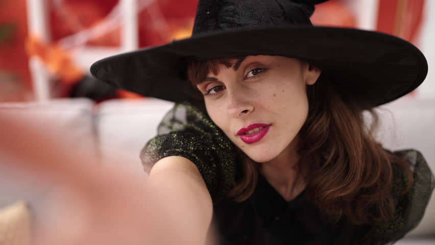 Young caucasian woman wearing witch costume make selfie by camera at home
