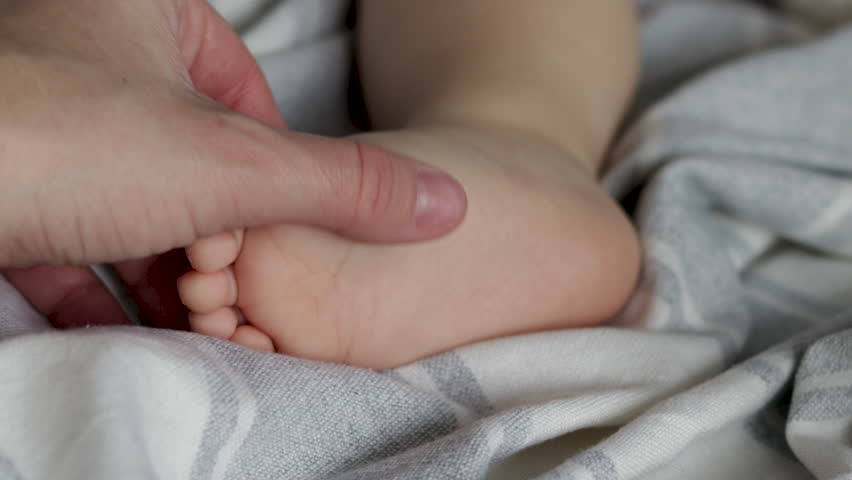 Baby feet toe under blanket cute toddler with shampoo shower gel bottle advertising video body infant child kid care.mother woman hand massaging boy feet.baby holding toes with cute small hands | Shutterstock HD Video #1100685573