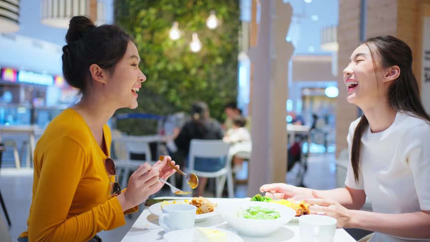 Asian beautiful women having dinner with friend in restaurant together. Attractive young girl feeling happy and relax, having fun talking and eating food at their table in dining room in cafeteria.