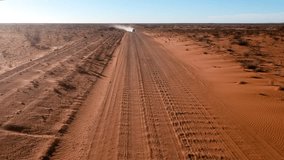 Cinematic drone video from car driving on outback road in red sand with dust australia