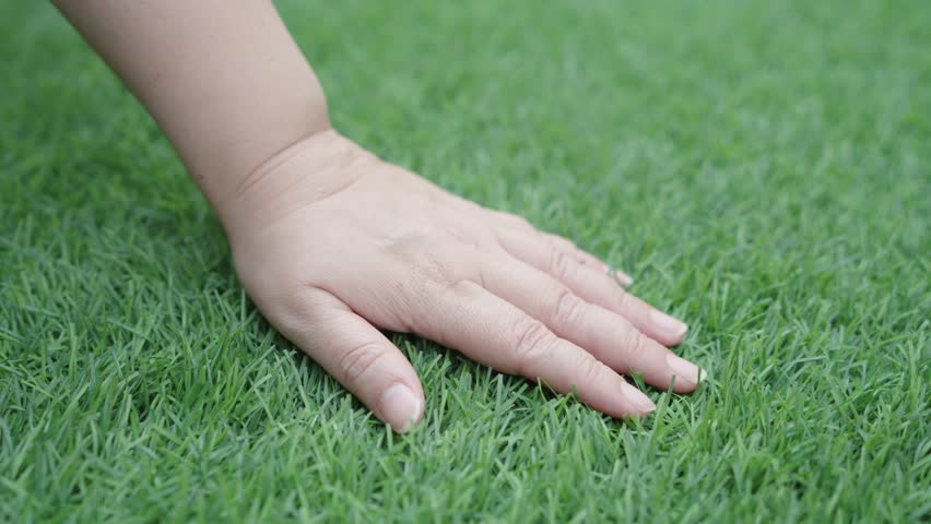 Female hand is touching artificial lawn grass. Hand on green grass. Feels the softness of artificial grass. Royalty-Free Stock Footage #1100692473