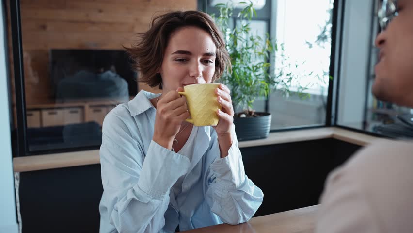 Funny brunette woman drinking tea and talking about work with her co-worker in the office | Shutterstock HD Video #1100694631