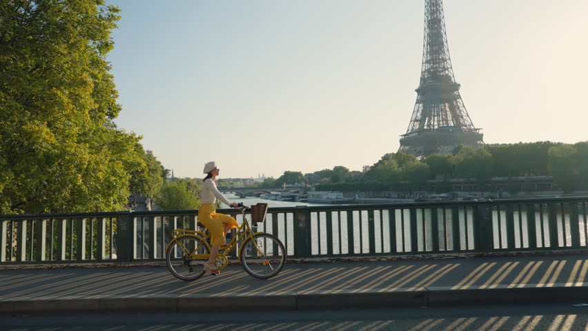 Pretty woman riding a yellow bicycle on a bridge overlooking the Eiffel Tower