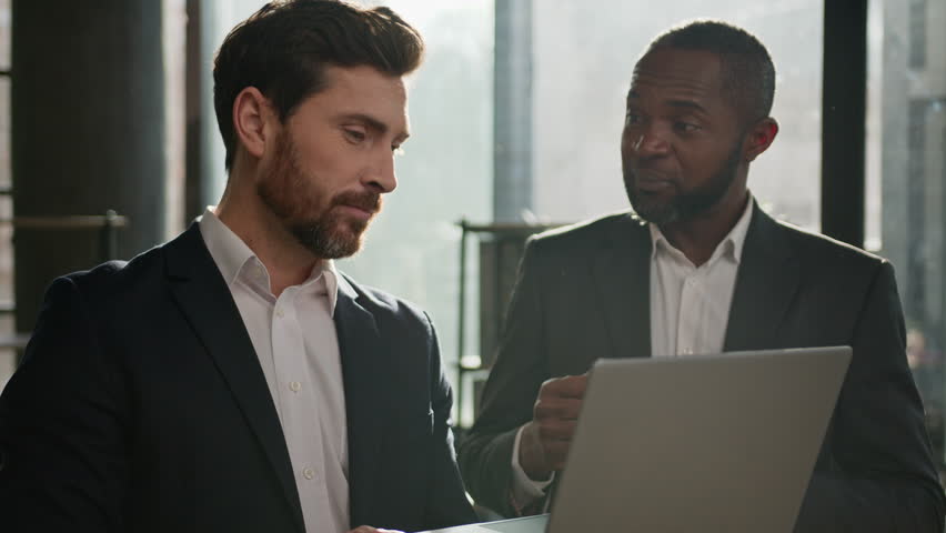 Caucasian man sales manager talking to African American male company client in office. Two diverse multiracial men employees workmates discuss business project software with laptop agree startup idea Royalty-Free Stock Footage #1100697225