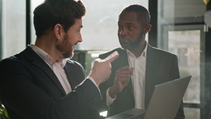 Caucasian man sales manager talking to African American male company client in office. Two diverse multiracial men employees workmates discuss business project software with laptop agree startup idea | Shutterstock HD Video #1100697225