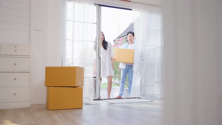 Asian young happy new marriage couple moving to new house together. Attractive romantic man and woman holding box parcel and suitcase with happiness and love. Family-Moving house relocation concept. Royalty-Free Stock Footage #1100698257
