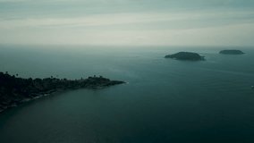 A long rocky coast with two islands on the horizon surrounded by boats and the deep blue sea. The color grading conveys a dramatic atmosphere in the footage.