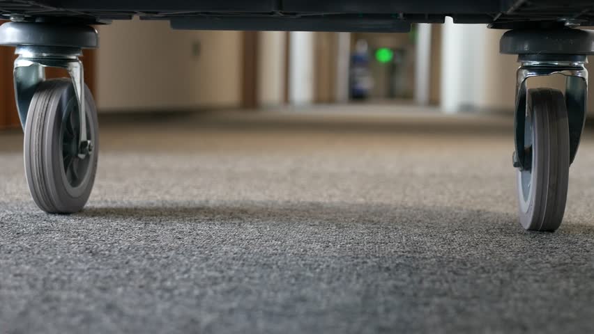 A close-up of the wheels of a guest luggage trolley in a hotel. The cart rolls down the hotel corridor at a low angle.