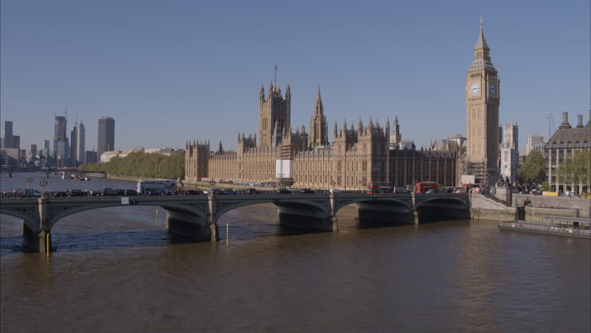 Aerial drone shot flying towards Westminster Bridge, Westminster Abbey and Big Ben over the River Thames with London Buses and traffic crossing Westminster Bridge on a bright clear sunny day. | Shutterstock HD Video #1100703883