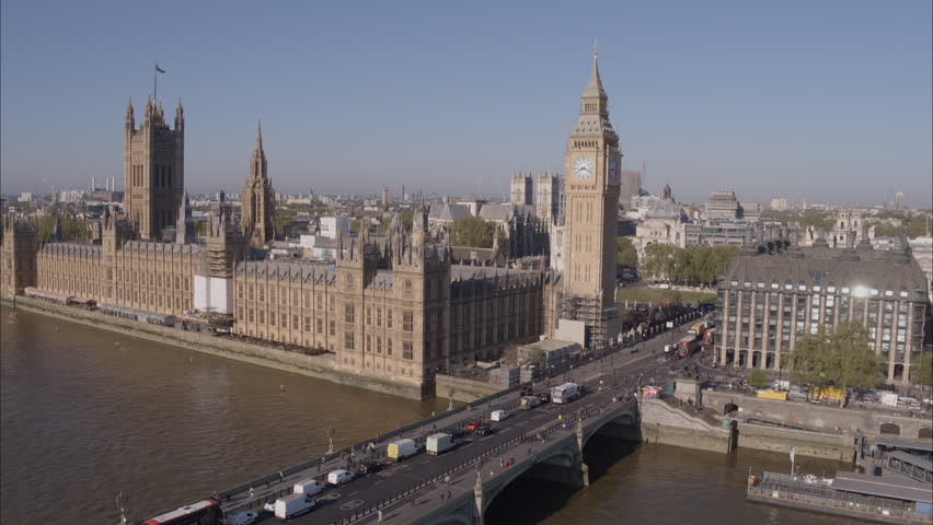 Aerial drone shot flying down and way from Westminster Bridge looking towards Westminster Abbey and Big Ben over the River Thames with traffic crossing Westminster Bridge on a bright clear sunny day. Royalty-Free Stock Footage #1100703903