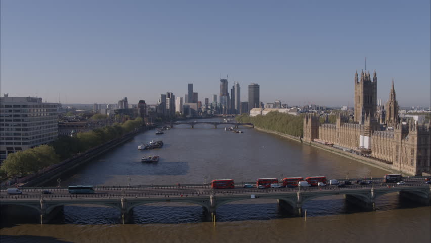 Aerial drone shot descending over Westminster Bridge looking south down River Thames on a bright clear sunny day with London buses over bridge and London skyline in background. | Shutterstock HD Video #1100703925