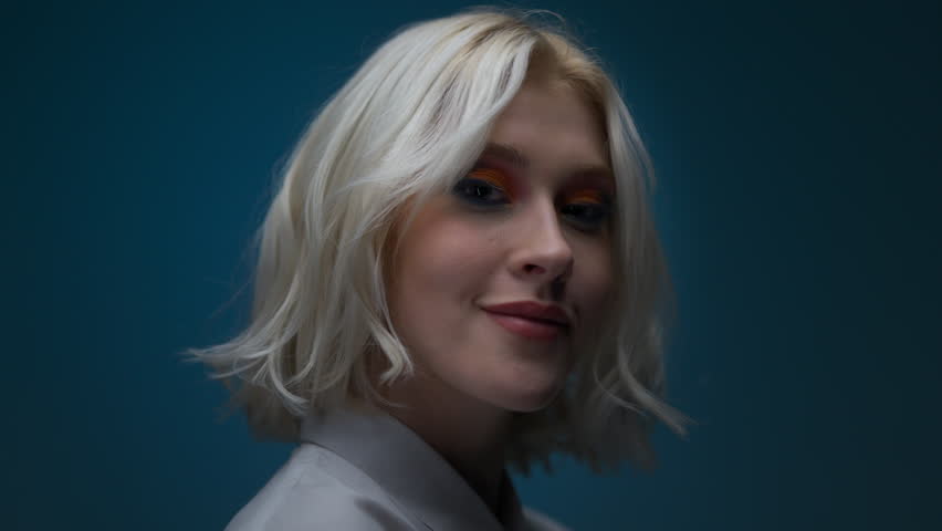 Portrait of blonde woman with bright makeup posing over blue colour wall in studio