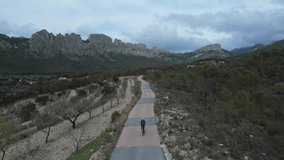 Woman is riding a road bike on a road between mountains,drone video, top view.Cycling in the mountains.Cycling adventure, a scenic ride through mountains. Finestrat, Alicante, Spain