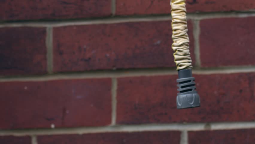 Gardener checks garden hose hangs against brick wall background medium zoom shot selective focus