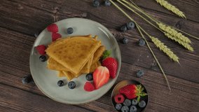 Taking a plate with French crepes served on plate with fresh strawberries and blueberries, woman's hands grabbing pancakes from wooden table, top view video clip, high quality 4k footage