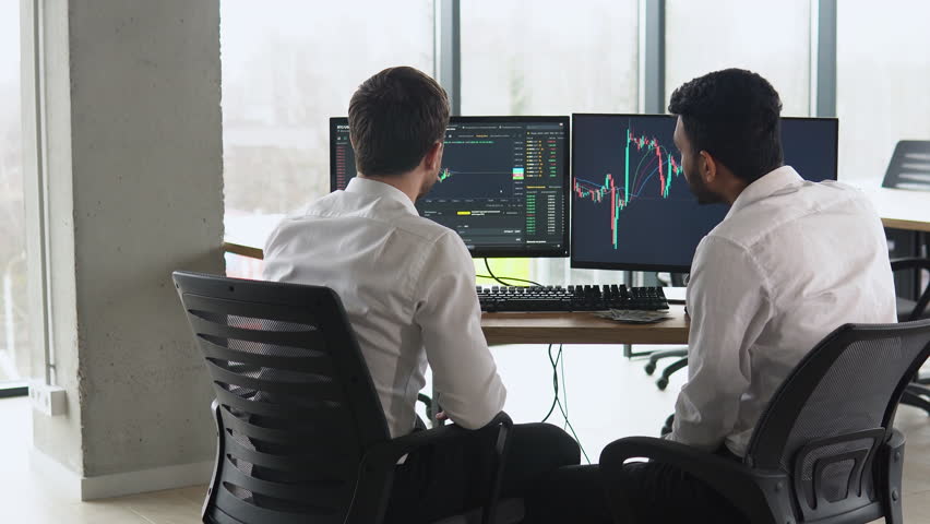 Two men traders sitting at desk at office together monitoring stocks data candle charts money flow on screen concentrated teamwork discussing strategy concept Royalty-Free Stock Footage #1100709951