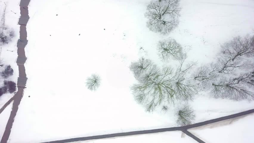 Aerial tracking shot above a city park and a residential building's yard covered in snow