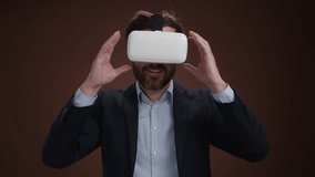 A man in a suit taking puttion on his vr headset with a happiness on his face. He is in a simple dark brown background. He looks amazed. High quality 4k footage - Powered by Shutterstock - Get 15% off with code: PIKWIZARD15