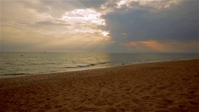 Romantic beach scene filmed just before sunset at dusk. This cloudy background video features a yellow sand beach in the Algarve, on the south coast of Portugal. There are attractive rays from the sun