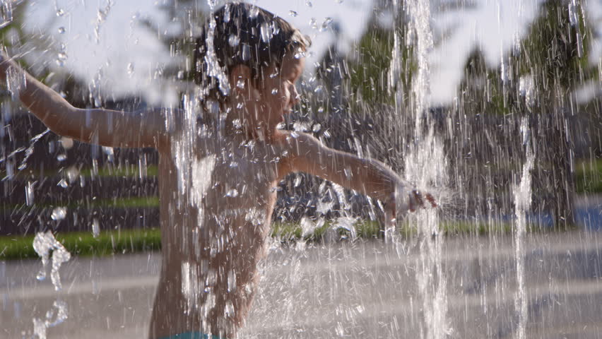 Carefree 6 year old boy dances, spins, splashes at community splash pad Royalty-Free Stock Footage #1100718231