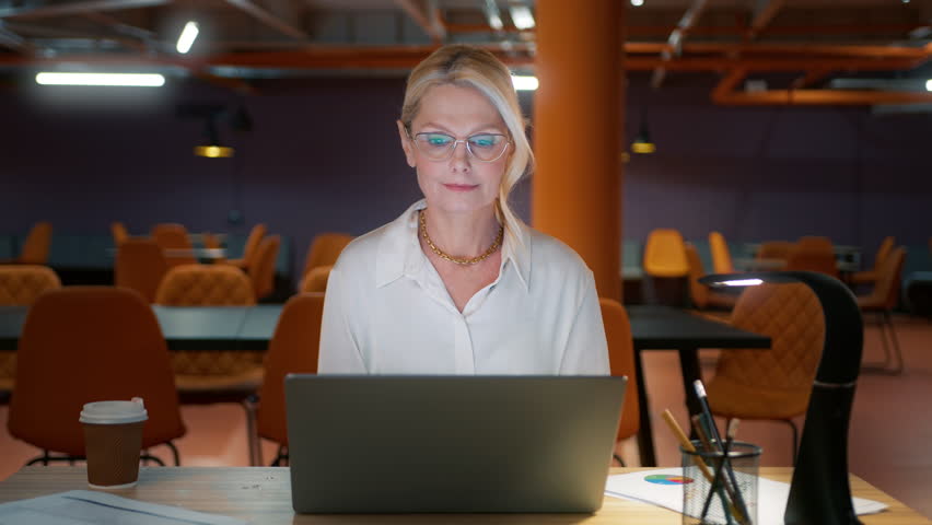Happy mature business woman wears stylish eyeglasses talks to web camera making distance online video conference call. Female doing distant International chat working after hours from office at night Royalty-Free Stock Footage #1100721249