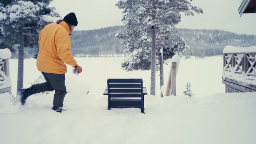 Man In Yellow Jacket With His Alaskan Malamute Dog Seated Outside Snow-Covered Yard. Static Shot