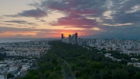 Cloudy sunset over Mirador Sur Park with cityscape of Santo Domingo in Dominican Republic. Aerial forward