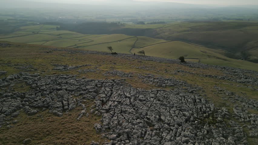 Distant hiker on rocky hillside with patchwork green fields and misty horizon at Ingleton Yorkshire UK