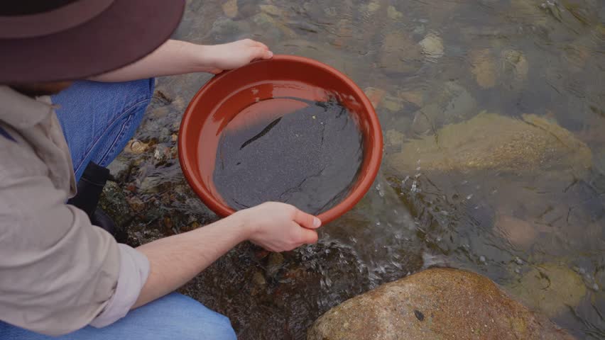 Gold pans in the hands of person in the hat a gold digger washing gold on the river,Finding gold