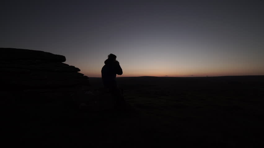 Dartmoor National Park, landscapes with hiker at dawn drinking tea looking at sunrise.