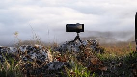 Travel vlogger start recording a time lapse with an expensive smart phone camera. Beautiful moving clouds from above. Unrecognizable geek man capturing amazing nature videos on a mountain peak. 4K