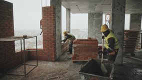 Long shot of African American construction worker mixing mortar paste and his Caucasian co-worker preparing reinforced block for further bricklaying work - Powered by Shutterstock - Get 15% off with code: PIKWIZARD15