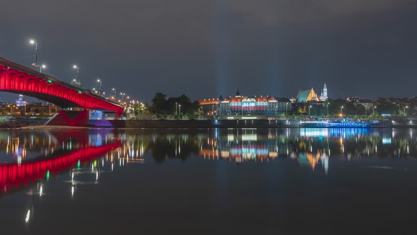 Night view time lapse of Warsaw. The Royal Castle, Old Town and glowing Śląsko-Dąbrowski Bridge  in Warsaw reflected in the Vistula River. 