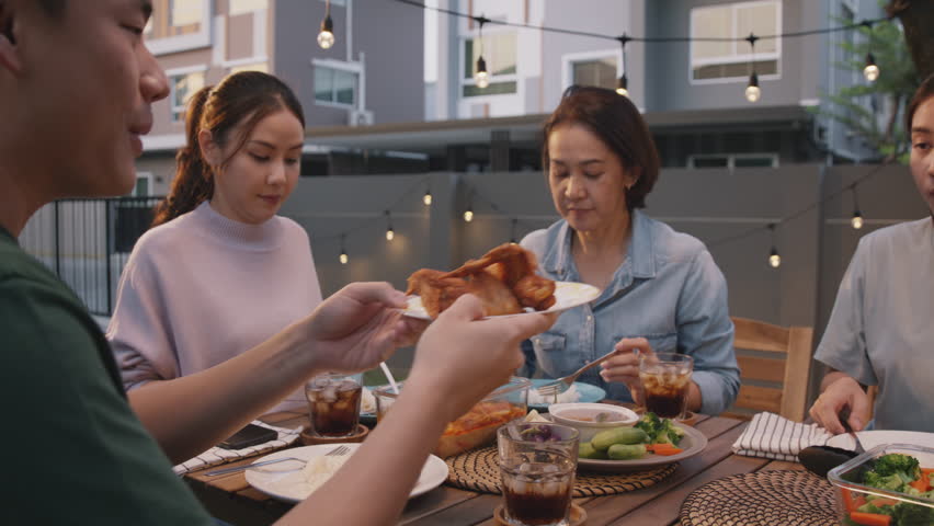 Mom enjoy thai meal cooking for family day home dining at dine table cozy patio. Mum passing serving food to group four asia people young adult man woman friend fun joy relax warm night picnic eating. Royalty-Free Stock Footage #1100732633