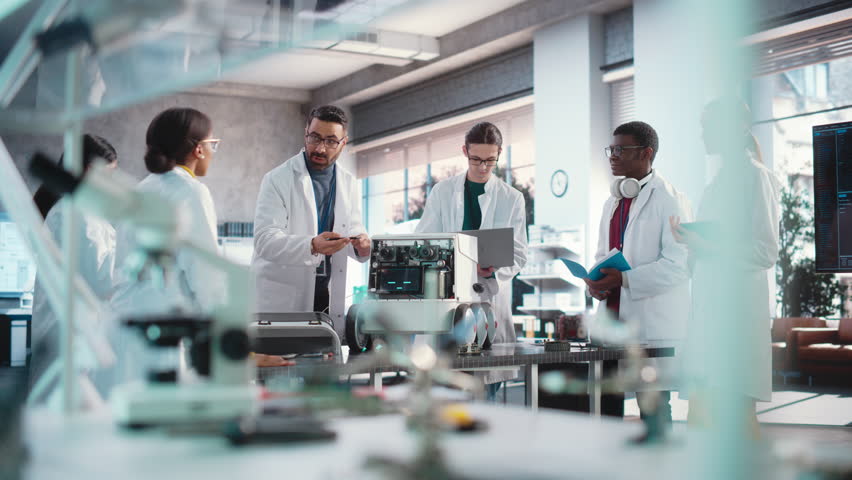 Diverse Team of Industrial Robotics Specialists Gathered Around a Table With a Mobile Robot. Engineers In Lab Coats Discussing an Automated AI Robotic Delivery Assistant, Using Laptop and Tablet Royalty-Free Stock Footage #1100736367