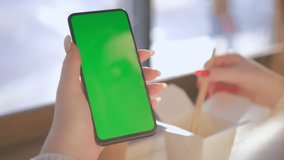 Young Woman in a chinese restaurant Sitting on a Couch with Green Screen Smartphone in Vertical Mode. Girl Using Smartphone, Browsing Internet, Watching Video Content, Blogs. POV. 4K