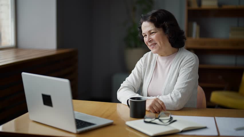 Happy woman smiling and waving hand, sitting in home and talking on video call using laptop camera. Online meeting with professional psychologist, freelance work, communication with beloved relatives. Royalty-Free Stock Footage #1100740891