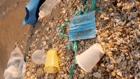 VERTICAL VIDEO, Close-up of disposable plastic, face mask and other debris on corals beach in surf zone. Plastic and other garbage on the seashore. Slow motion