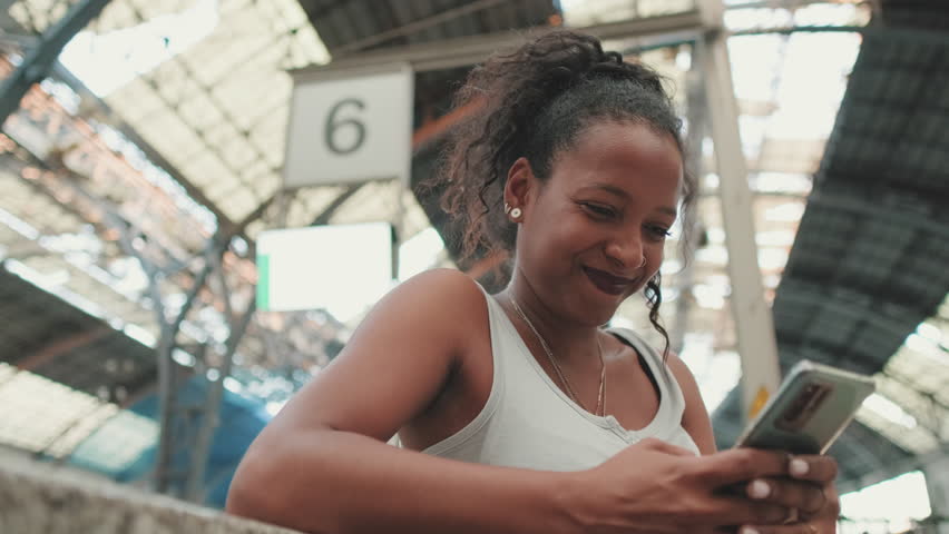 Close up, young woman sitting at the railway station, using cellphone